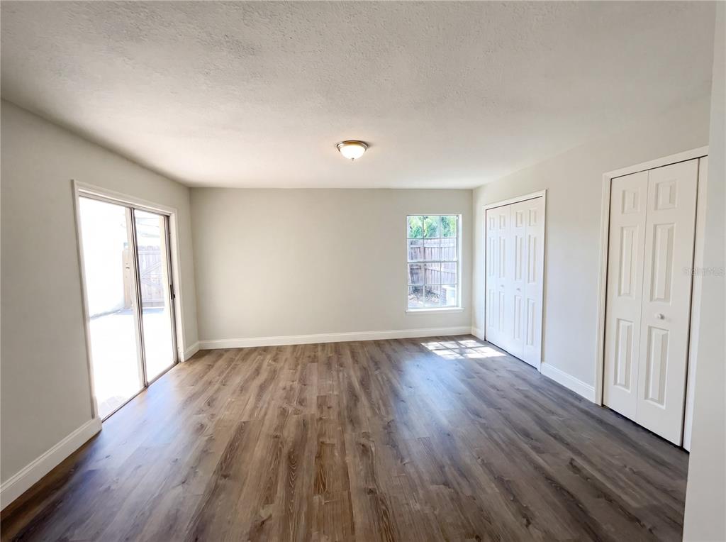An empty room with wood-look flooring, a sliding glass door, a window, and two closets — 780 OLYMPIC CIRCLE UNIT I3, OCOEE, FL
