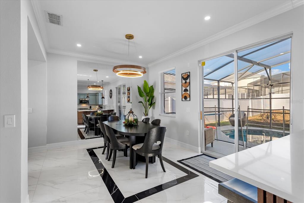 A dining room with a dark table, modern chandelier, and sliding doors overlooking a pool — 117 FOREST VIEW COURT, DAVENPORT, FL