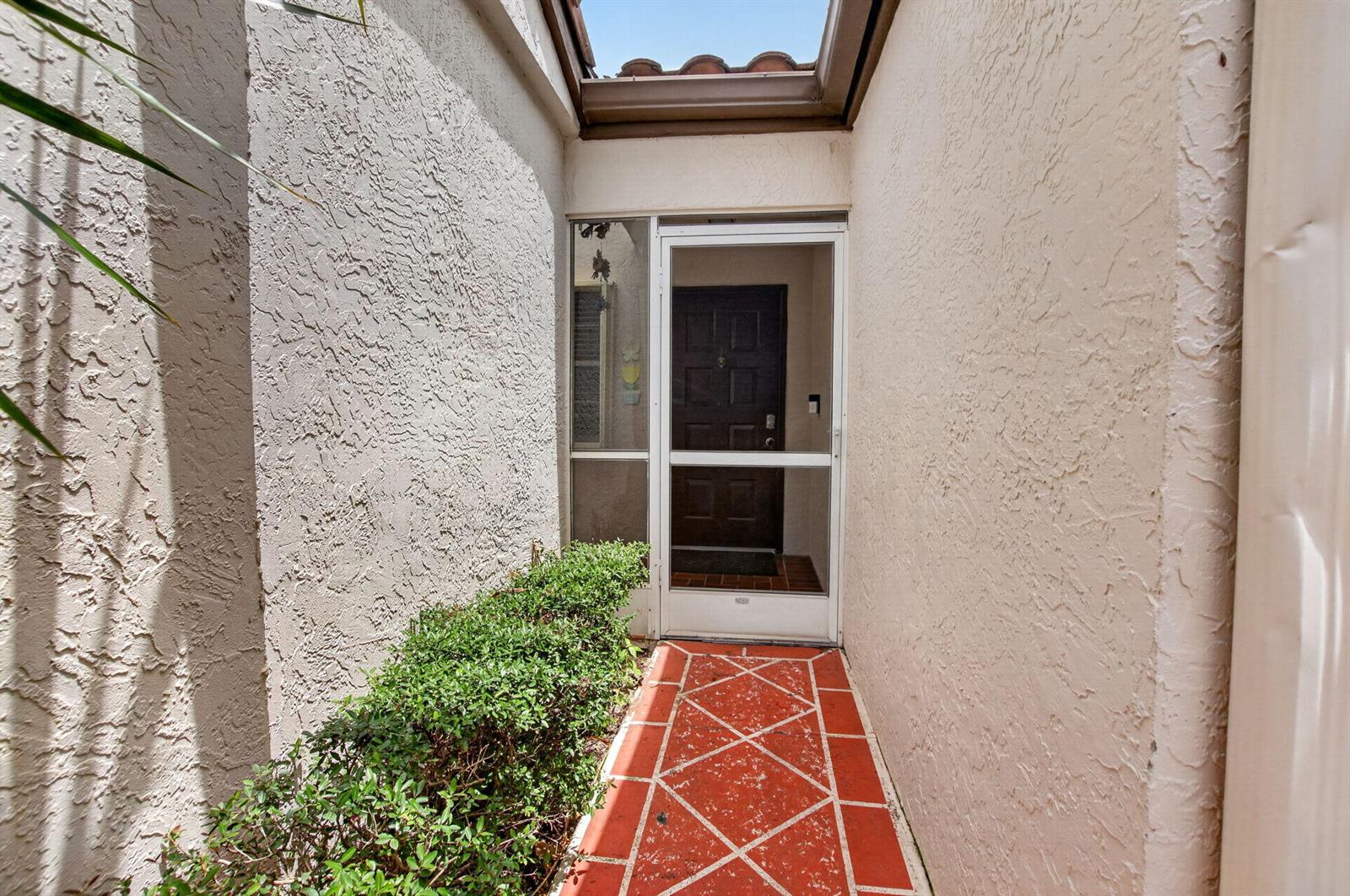 A narrow entryway features a screen door, a tiled walkway, and stucco walls — 6082 Waldwick Circle, Delray Beach FL 33484, DELRAY BEACH, FL
