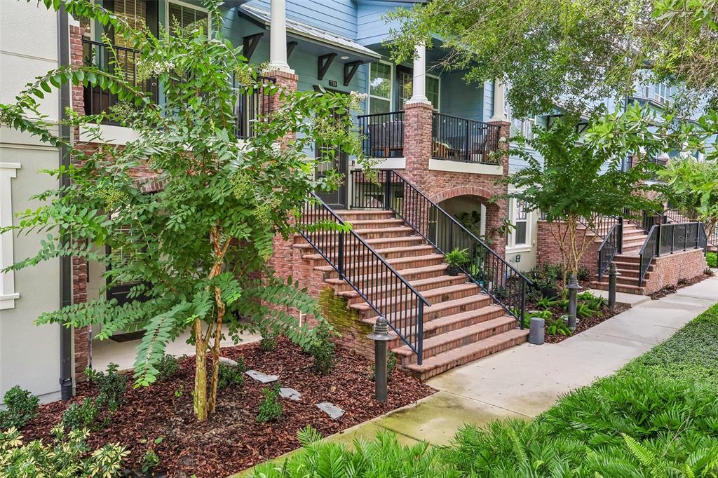 A multi-story townhouse exterior features brick stairs leading to a raised porch with black railings — 714 CATALONIA COVE, OVIEDO, FL