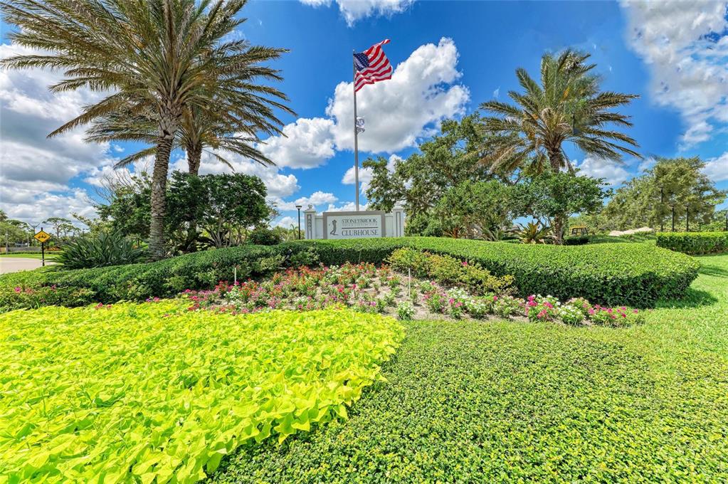 A landscaped entrance sign for Stoneybrook Clubhouse features a flagpole and palm trees under clouds — 9560 HIGH GATE DRIVE UNIT 1626, SARASOTA, FL