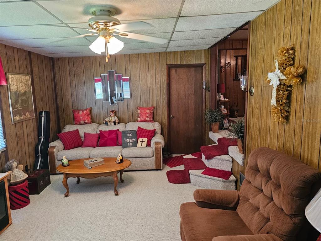 A living room features wood-paneled walls, a beige sofa, a brown recliner, and carpeted flooring — 14655 SE 47TH COURT, SUMMERFIELD, FL