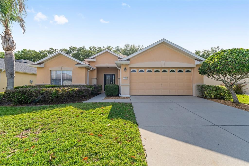 A single-story house with a beige stucco exterior, a two-car garage, and a front lawn — 13358 SE 86TH CIRCLE, SUMMERFIELD, FL