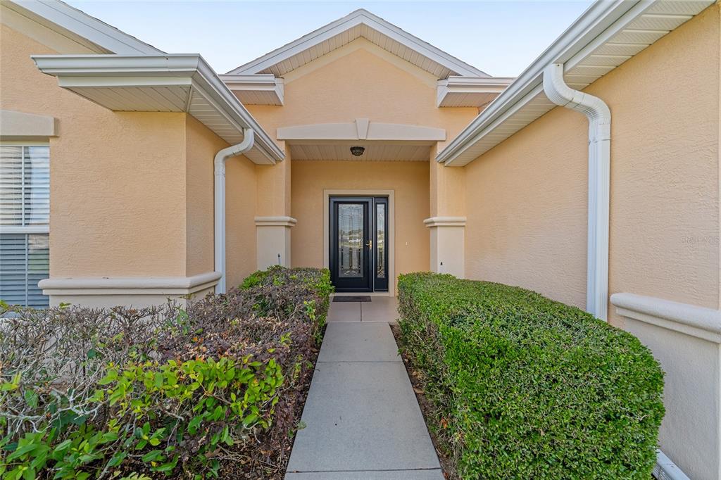 A concrete walkway leads to the front entrance of a beige house with trimmed hedges — 13358 SE 86TH CIRCLE, SUMMERFIELD, FL