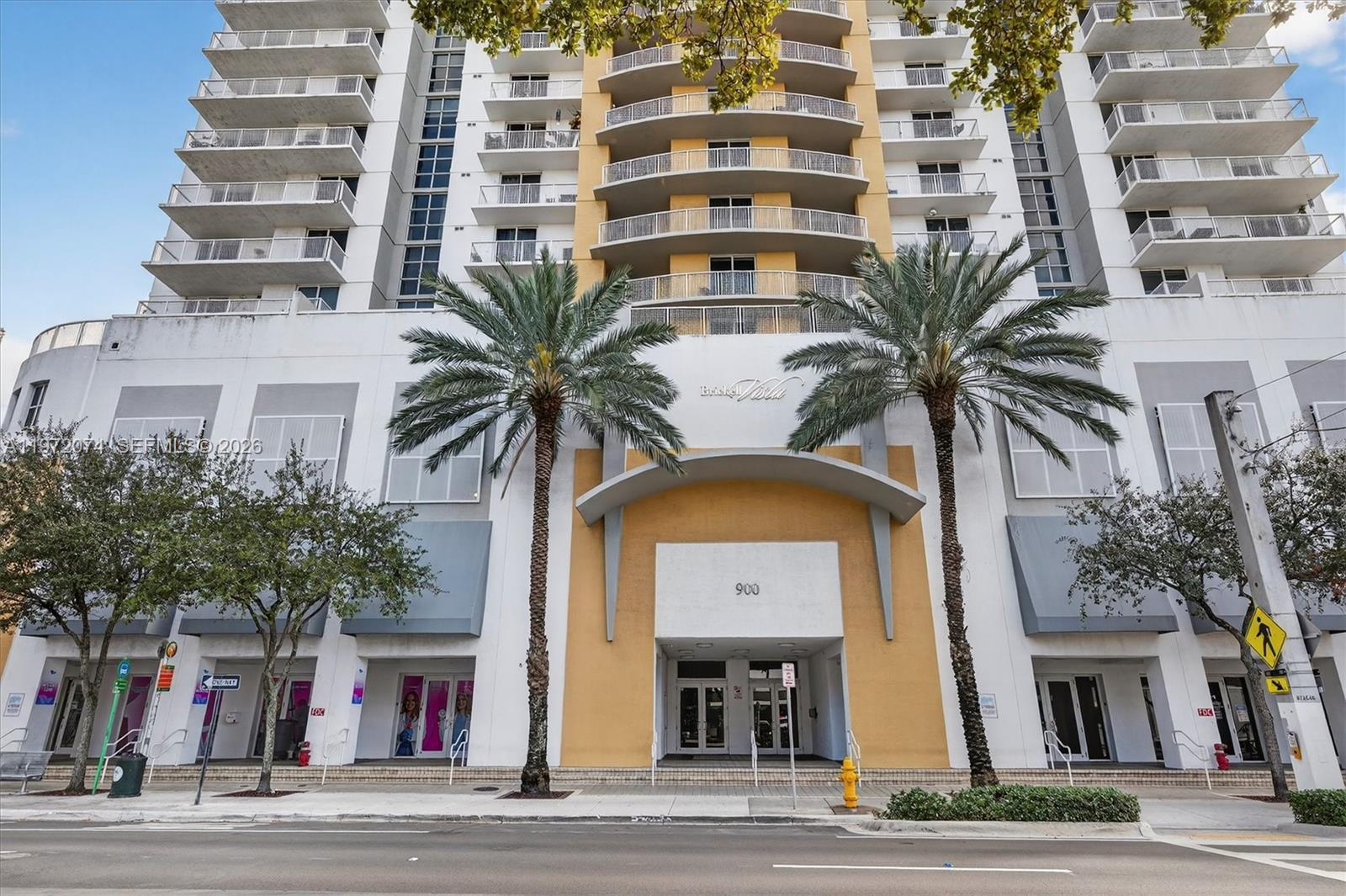 A low-angle exterior view of a multi-story residential building with palm trees at the entrance — 900 SW 8th St # 505, Miami FL 33130, MIAMI, FL