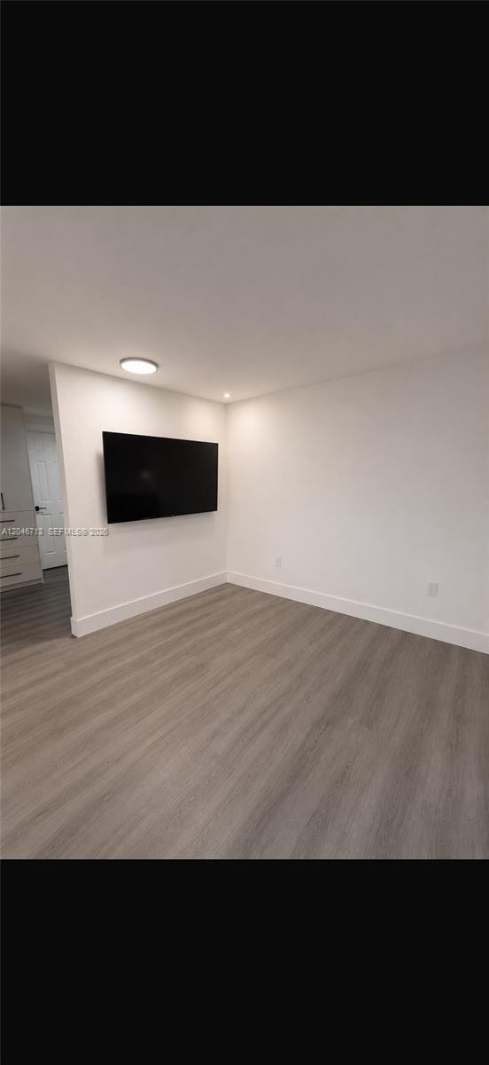 A minimalist room features light wood-look flooring, white walls, and a wall-mounted television — 14321 Madison St # 1, Miami FL 33176, MIAMI, FL