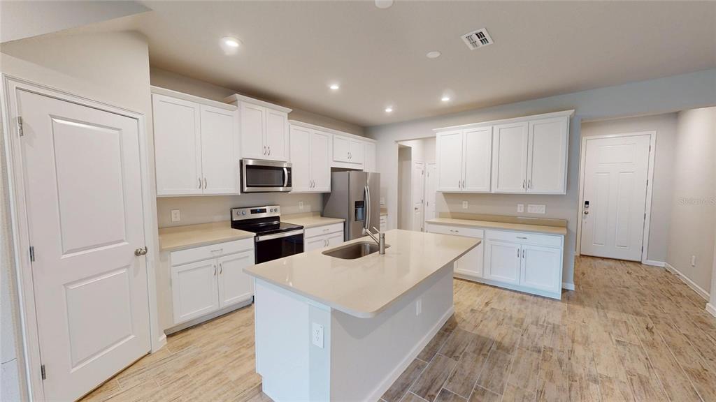 A kitchen with white cabinets, a central island, stainless steel appliances, and light wood flooring — 26130 FANTASY SKY LANE, LUTZ, FL