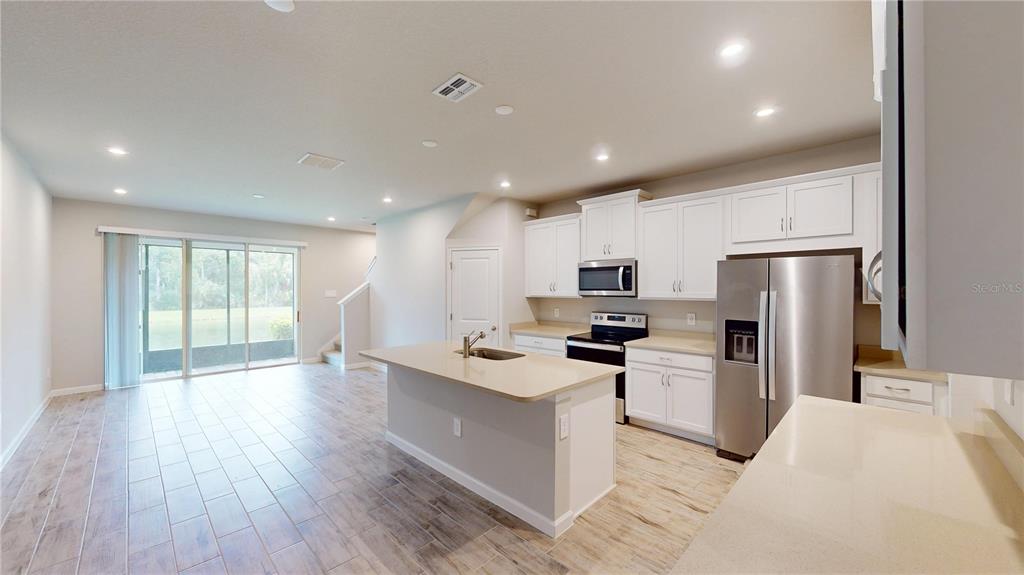 A kitchen with white cabinets, stainless steel appliances, and an island overlooks a living area — 26130 FANTASY SKY LANE, LUTZ, FL