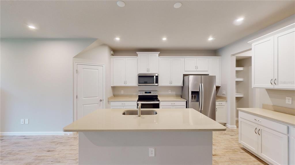 A kitchen features white cabinets, stainless steel appliances, a center island, and light-colored flooring — 26130 FANTASY SKY LANE, LUTZ, FL