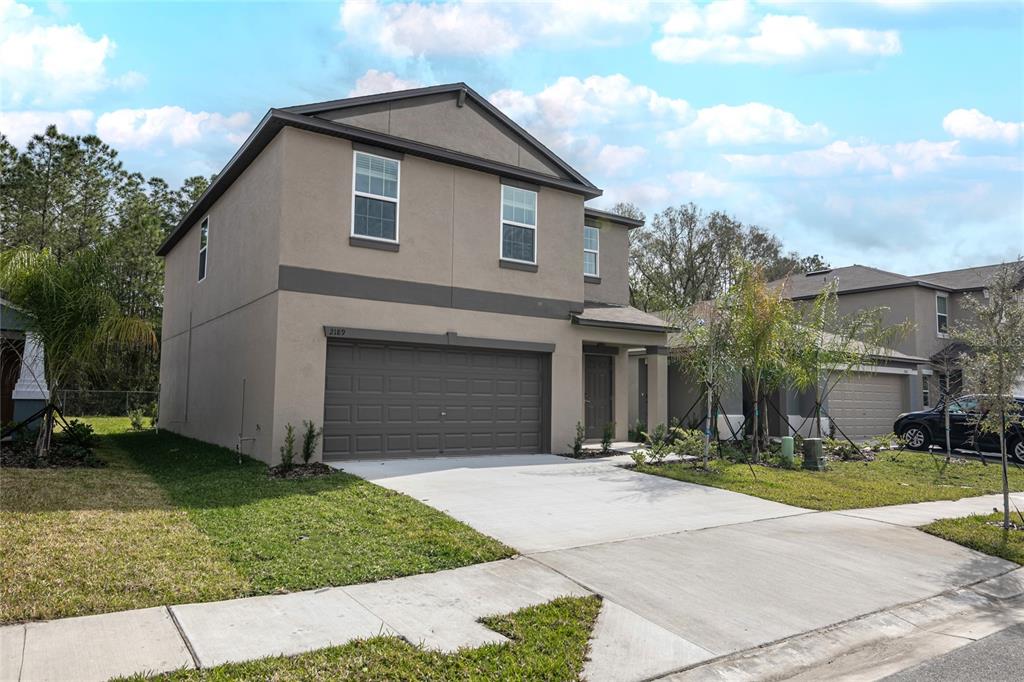 A two-story suburban house with a tan stucco exterior, a two-car garage, and a driveway — 2189 TENEROC TRAIL, LAKELAND, FL