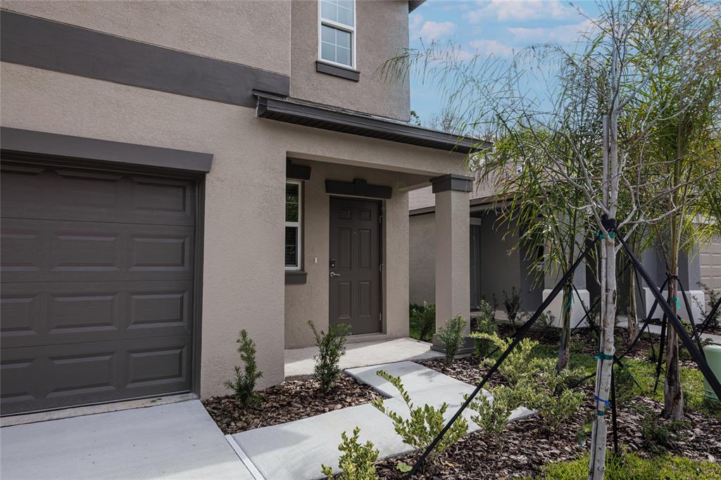 A tan two-story house exterior features a brown garage door, front door, and small landscaping — 2189 TENEROC TRAIL, LAKELAND, FL