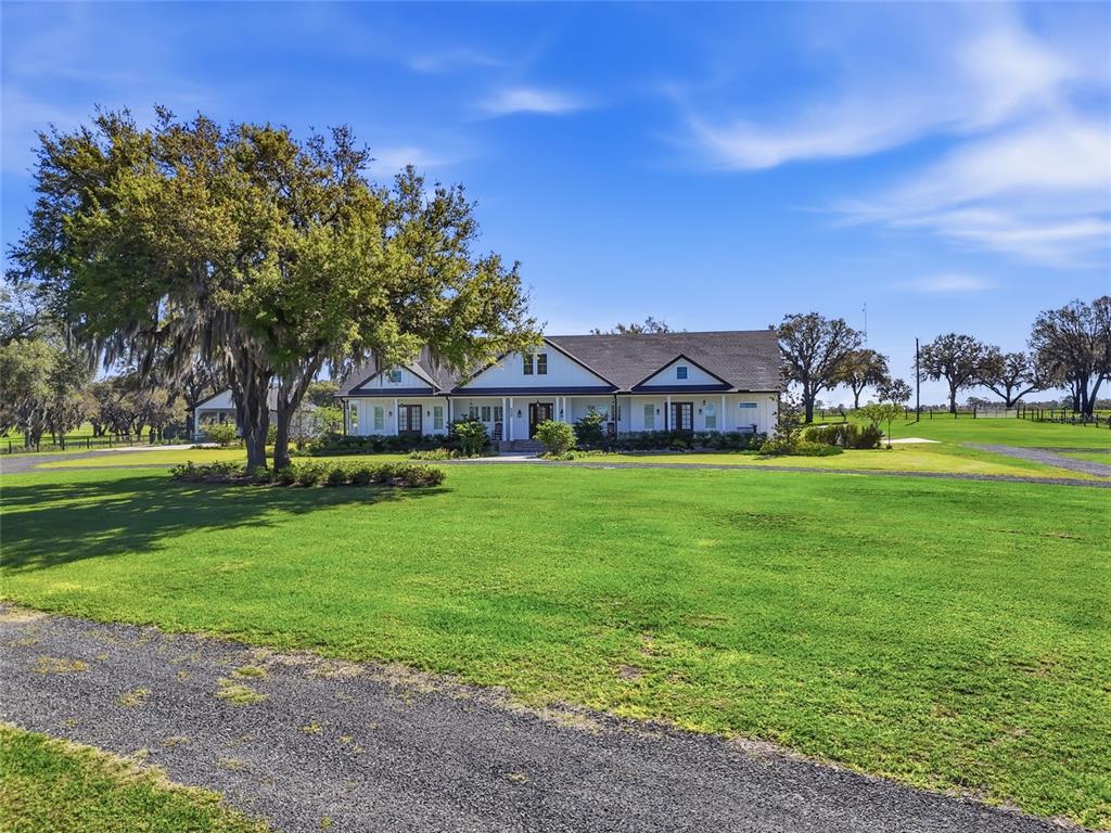 A white farmhouse with a dark roof sits behind a large lawn and gravel driveway — 11131 NE 35TH STREET, BRONSON, FL
