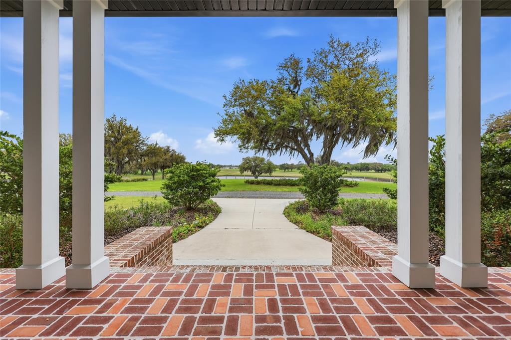 A brick porch with white columns overlooks a concrete walkway, green lawn, and large trees — 11131 NE 35TH STREET, BRONSON, FL