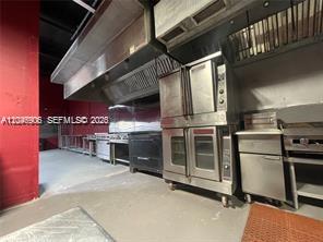 A commercial kitchen features stainless steel ovens, a large ventilation hood, and red walls — 2739 NW 54th St, Miami FL 33142, MIAMI, FL