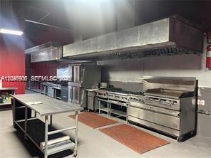 A commercial kitchen features stainless steel appliances, a large exhaust hood, and a metal prep table — 2739 NW 54th St, Miami FL 33142, MIAMI, FL