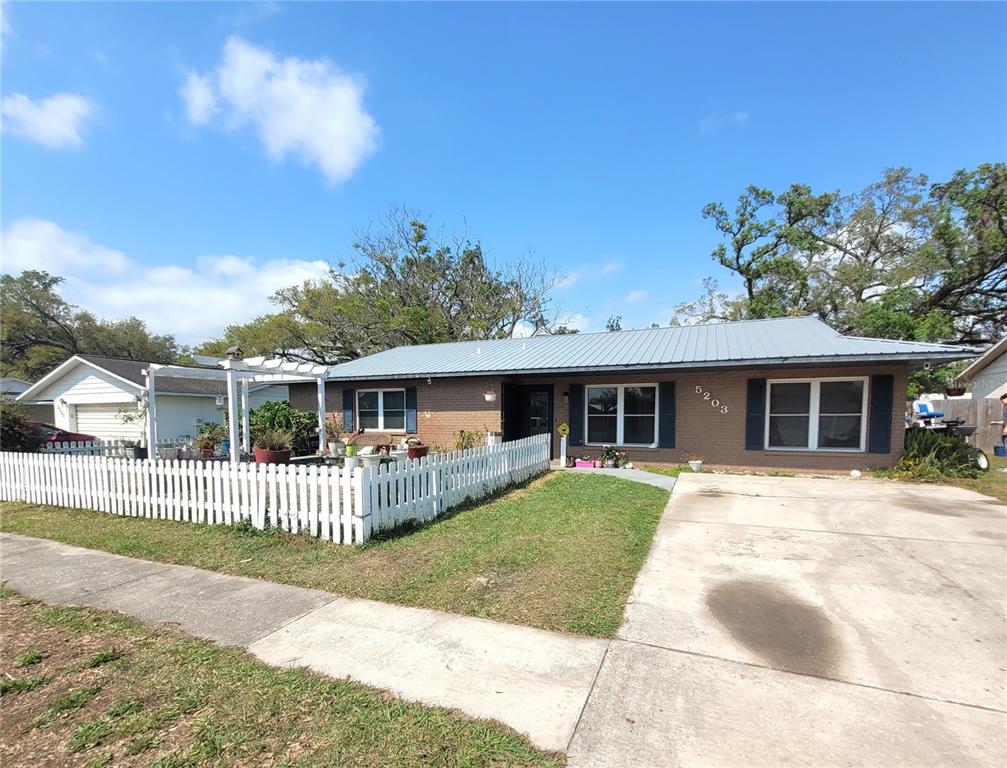 A single-story brick house features a metal roof, a white picket fence, and a driveway — 5203 PRESIDENTIAL STREET, SEFFNER, FL