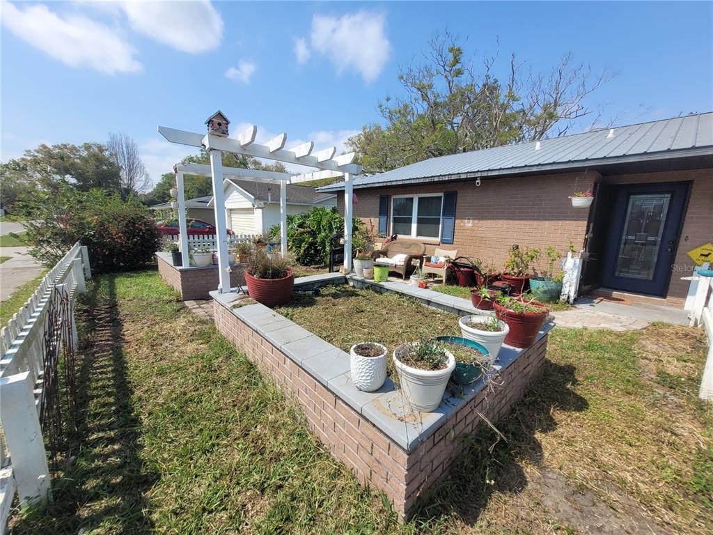 A brick house features a raised garden bed with a white pergola in the front yard — 5203 PRESIDENTIAL STREET, SEFFNER, FL
