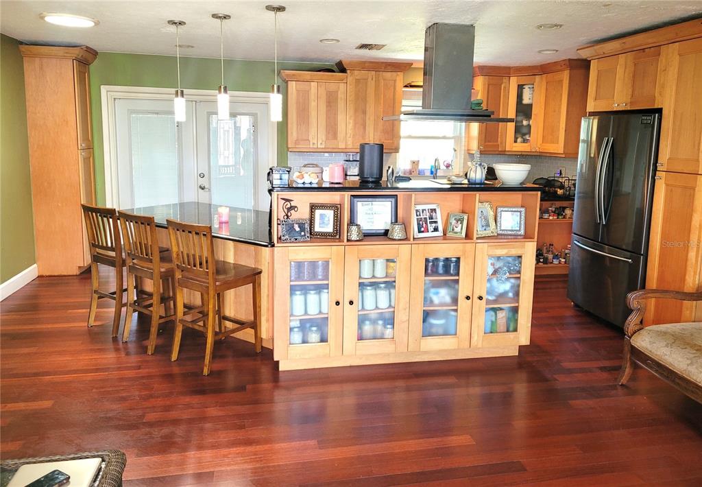 A kitchen features wood cabinets, a black countertop island with seating, and dark hardwood floors — 5203 PRESIDENTIAL STREET, SEFFNER, FL