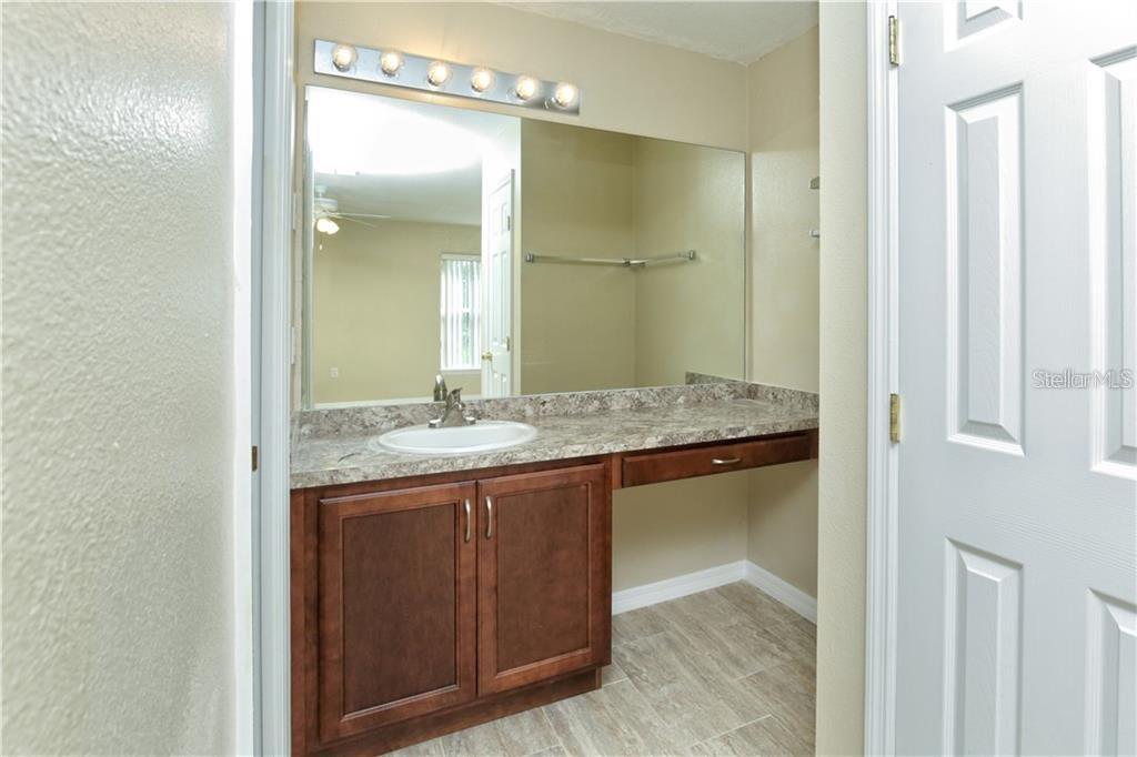 A bathroom features a vanity with a stone countertop, a mirror, and wood cabinets — 8829 GRAND PALMS CIRCLE UNIT A, KISSIMMEE, FL
