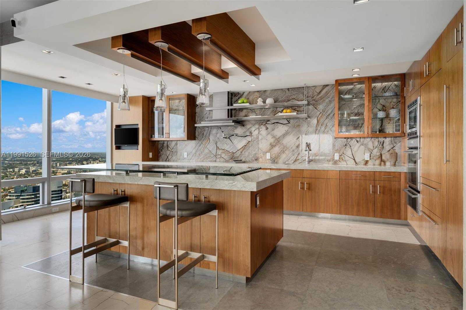 A modern kitchen features wood cabinetry, a stone island with bar stools, and floor-to-ceiling windows — 1425 Brickell Ave, Miami FL 33131, MIAMI, FL