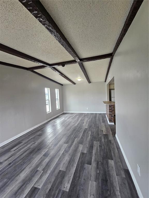 An empty living room features gray wood-look flooring, a popcorn ceiling with dark wooden beams — 3037 SAINT PAUL DRIVE, WINTER HAVEN, FL