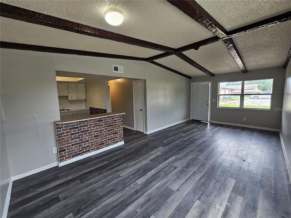 A living room features dark wood-look flooring, a brick breakfast bar, and exposed ceiling beams — 3037 SAINT PAUL DRIVE, WINTER HAVEN, FL