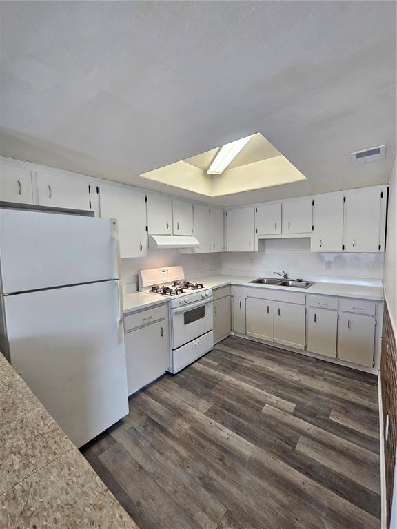 A kitchen with white cabinets, white appliances, a skylight, and wood-look flooring — 3037 SAINT PAUL DRIVE, WINTER HAVEN, FL