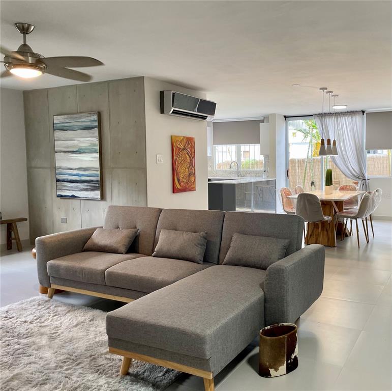 A living room with a gray sectional sofa, concrete-style wall panels, and an adjacent dining area — 290 SANTA ANA AVENUE, GUAYNABO, PR