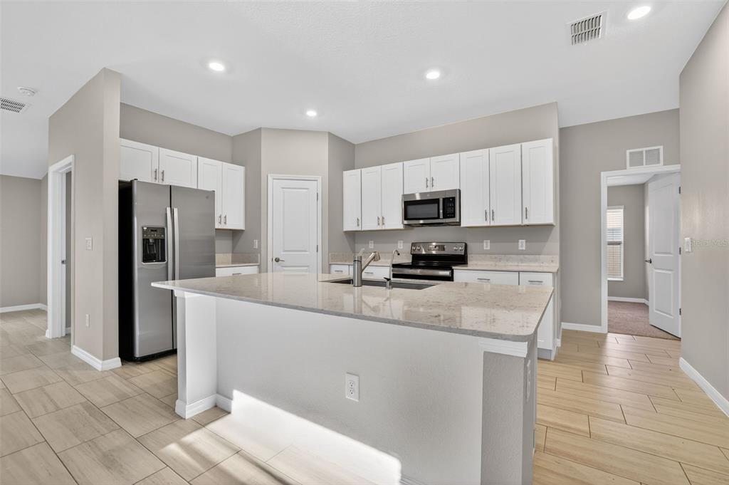A modern kitchen features white cabinets, granite countertops, a center island, and stainless steel appliances — 13187 PALMERSTON ROAD, RIVERVIEW, FL