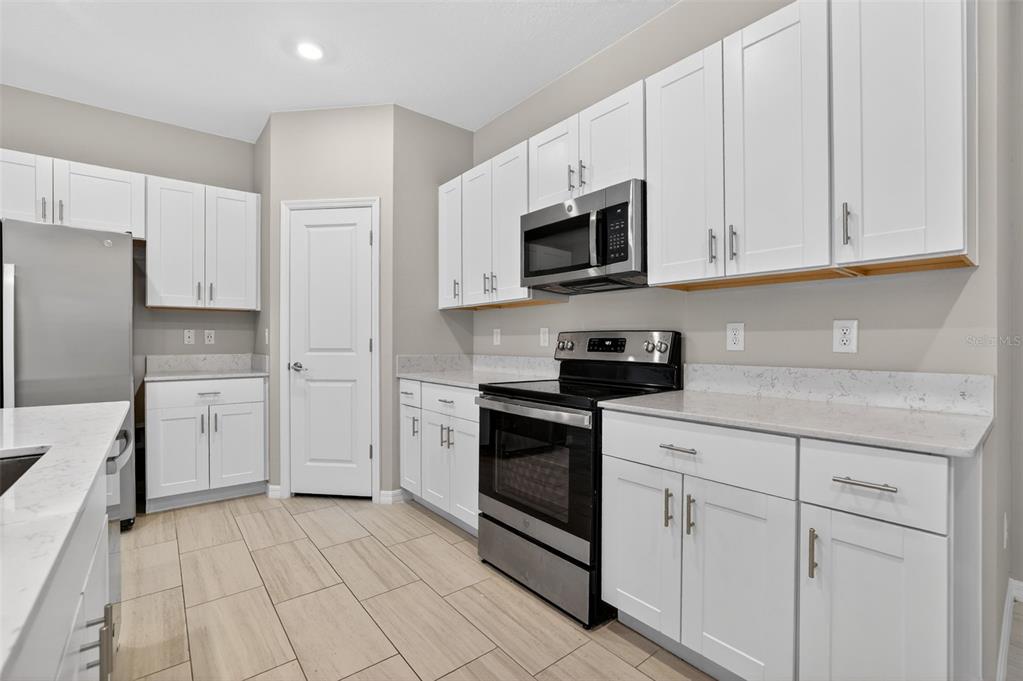 A kitchen features white cabinets, stainless steel appliances, and light-colored countertops with tile flooring — 13187 PALMERSTON ROAD, RIVERVIEW, FL