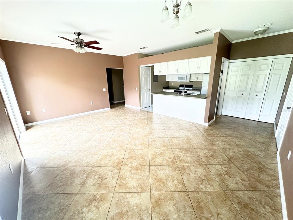 A spacious room features tan tile flooring, brown walls, a ceiling fan, and a kitchen area — 1003 EAGLE POND DRIVE UNIT 1003, WINTER HAVEN, FL