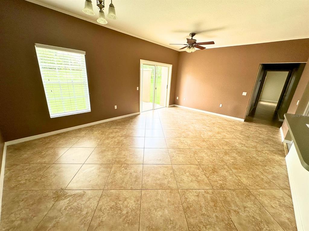 A spacious living room features brown walls, tile flooring, a ceiling fan, and sliding glass doors — 1003 EAGLE POND DRIVE UNIT 1003, WINTER HAVEN, FL
