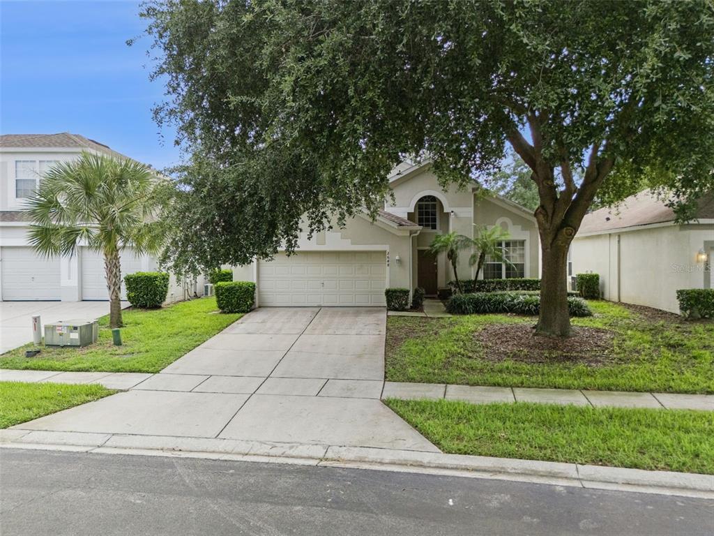 A single-story house with a two-car garage, a concrete driveway, and a large front tree — 2648 DAULBY STREET, KISSIMMEE, FL