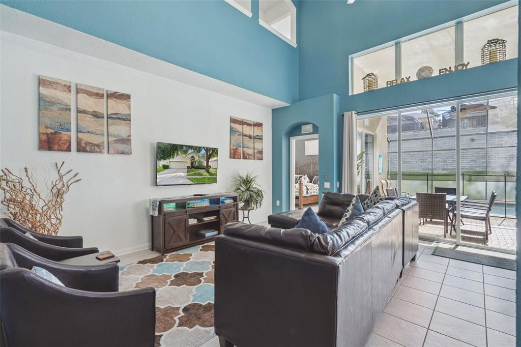 A living room features high blue ceilings, a television, a sectional sofa, and sliding doors — 2648 DAULBY STREET, KISSIMMEE, FL