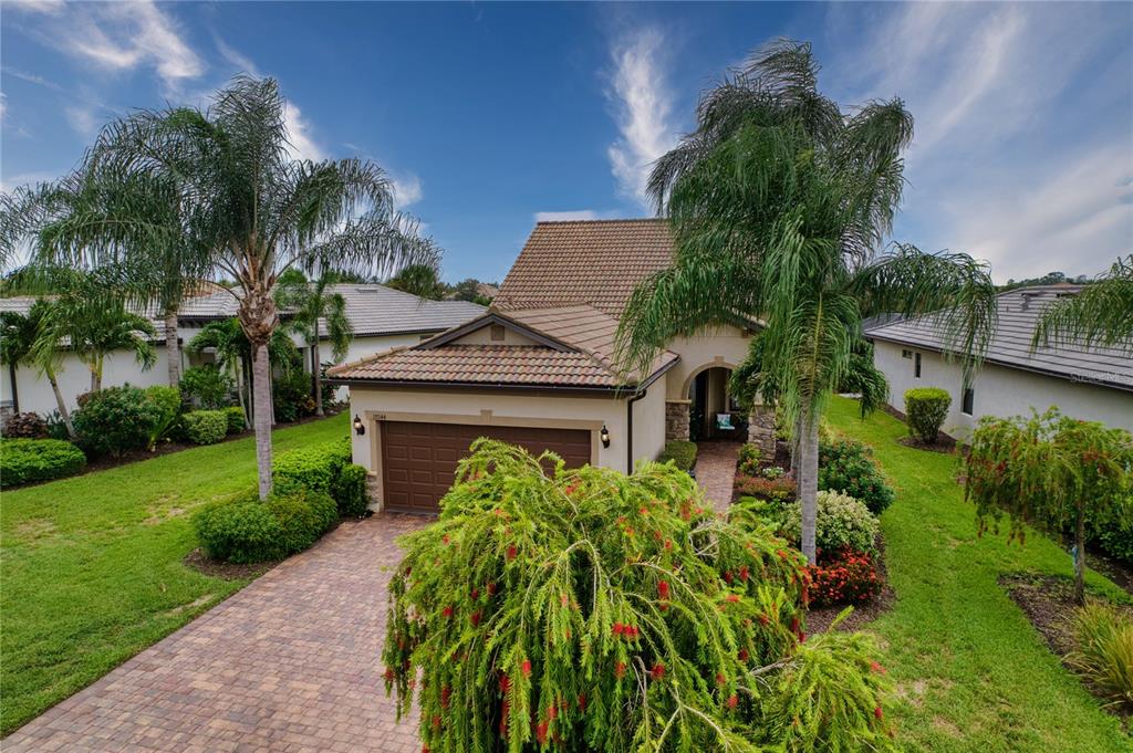 A single-story house with a brown tile roof, a brick driveway, and lush landscaping — 17044 KENTON TERRACE, BRADENTON, FL