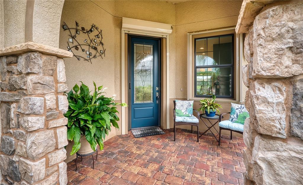 A stone-columned porch features a blue front door, a potted plant, and two patio chairs — 17044 KENTON TERRACE, BRADENTON, FL