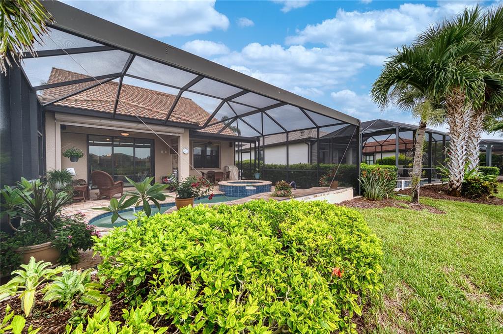 A screened-in patio features a swimming pool, a hot tub, and lush landscaping — 17044 KENTON TERRACE, BRADENTON, FL