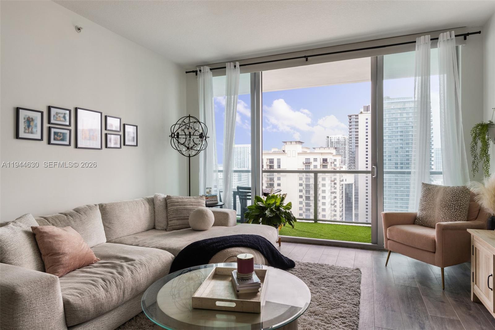 A living room features a beige sectional sofa, a glass coffee table, and a balcony view — 1111 SW 1st Ave, Miami FL 33130, MIAMI, FL