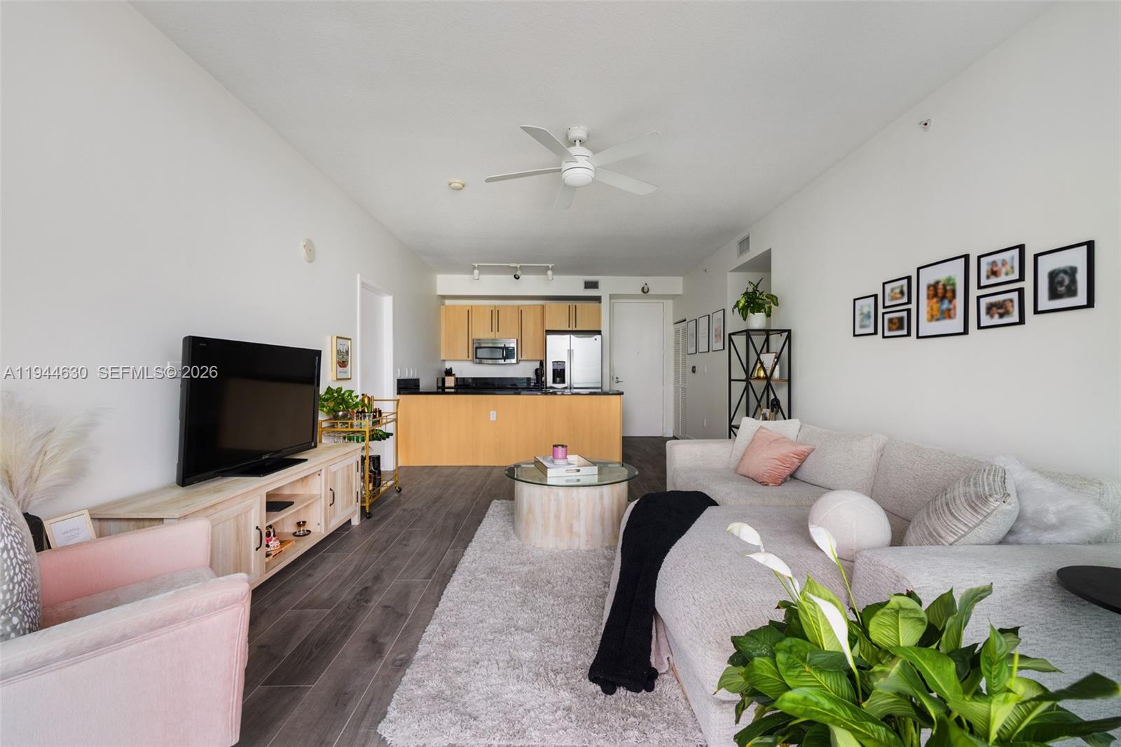 A living room with a sectional sofa, television, and an open kitchen with wood cabinets — 1111 SW 1st Ave, Miami FL 33130, MIAMI, FL