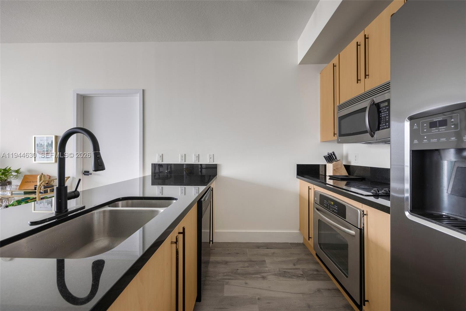 A modern kitchen features light wood cabinets, black countertops, stainless steel appliances, and gray flooring — 1111 SW 1st Ave, Miami FL 33130, MIAMI, FL