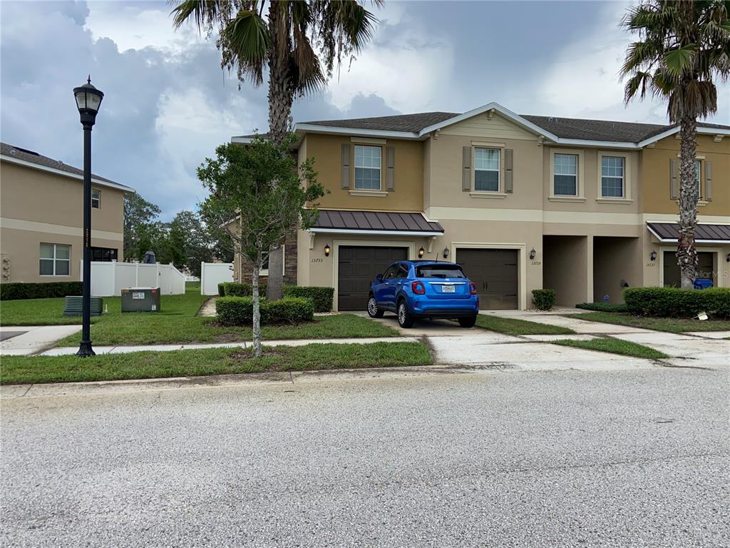 A blue car is parked in front of a two-story townhouse with a brown garage — 13733 ROSETTE ROAD, HUDSON, FL