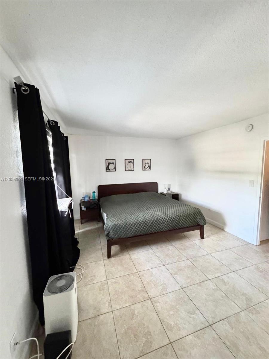A bedroom features a dark bed frame, tiled flooring, and black curtains — 1100 Alton Rd # 5D, Miami Beach FL 33139, MIAMI BEACH, FL