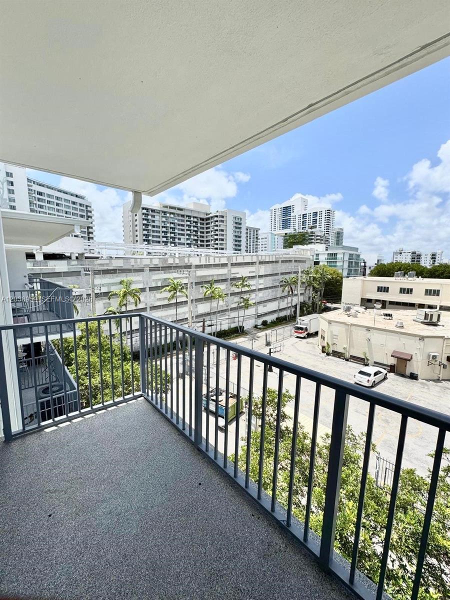 A balcony with a gray floor and metal railing overlooks a parking lot and buildings — 1100 Alton Rd # 5D, Miami Beach FL 33139, MIAMI BEACH, FL
