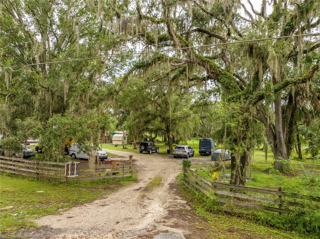 A dirt driveway leads through a wooden fence into a wooded area with several parked vehicles — 36720 EMERALDA ISLAND ROAD, LEESBURG, FL