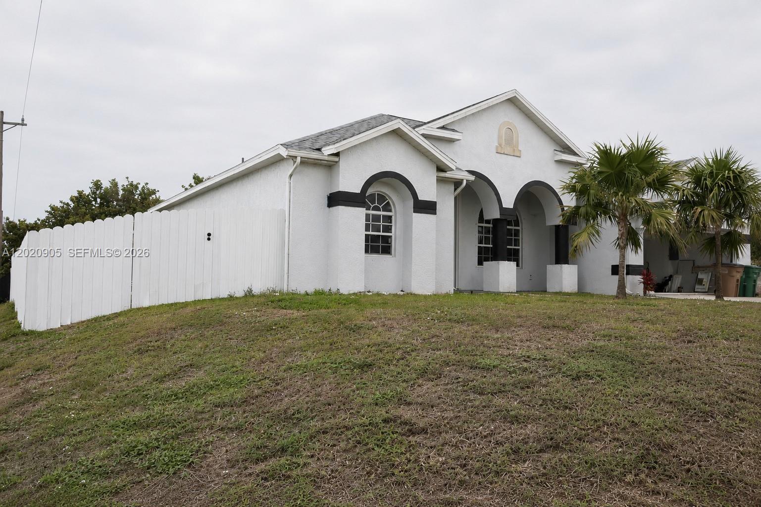 A white stucco house with arched windows and a white fence sits on a grassy hill — 1602 SW 14th St, Cape Coral FL 33991, CAPE CORAL, FL