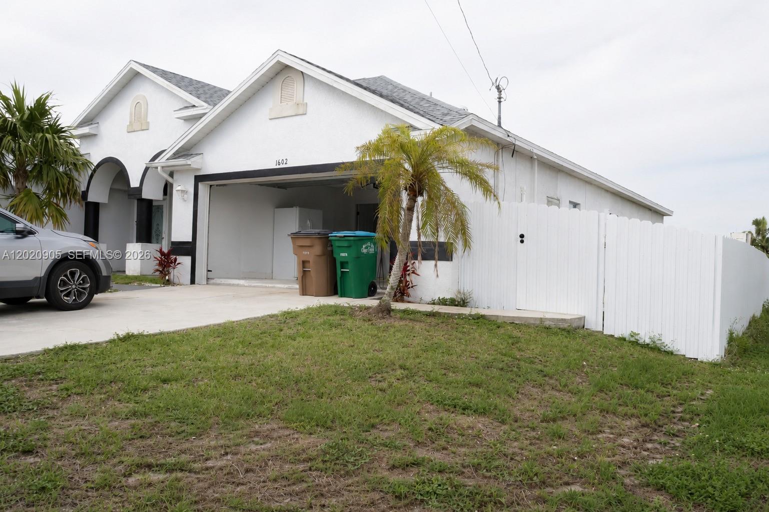 A white house exterior features a garage, a palm tree, and a white privacy fence — 1602 SW 14th St, Cape Coral FL 33991, CAPE CORAL, FL