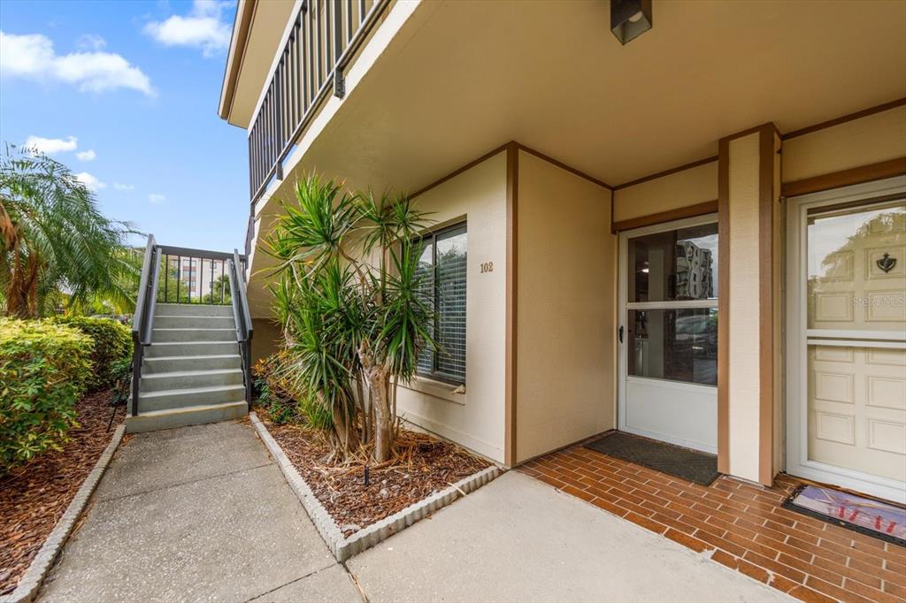 An exterior view of a ground-floor apartment entrance with stairs leading to an upper level — 6219 PALMA DEL MAR BOULEVARD S UNIT 102, ST PETERSBURG, FL