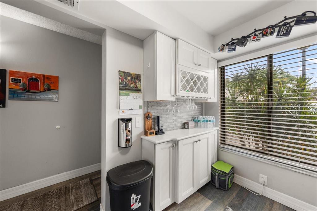 A white wet bar with glass-front cabinets and a tiled backsplash sits by a window — 6219 PALMA DEL MAR BOULEVARD S UNIT 102, ST PETERSBURG, FL