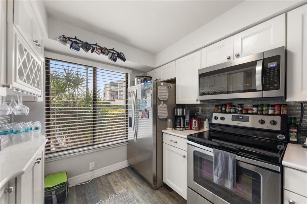 A kitchen features white cabinets, stainless steel appliances, a window with blinds, and wood-look flooring — 6219 PALMA DEL MAR BOULEVARD S UNIT 102, ST PETERSBURG, FL