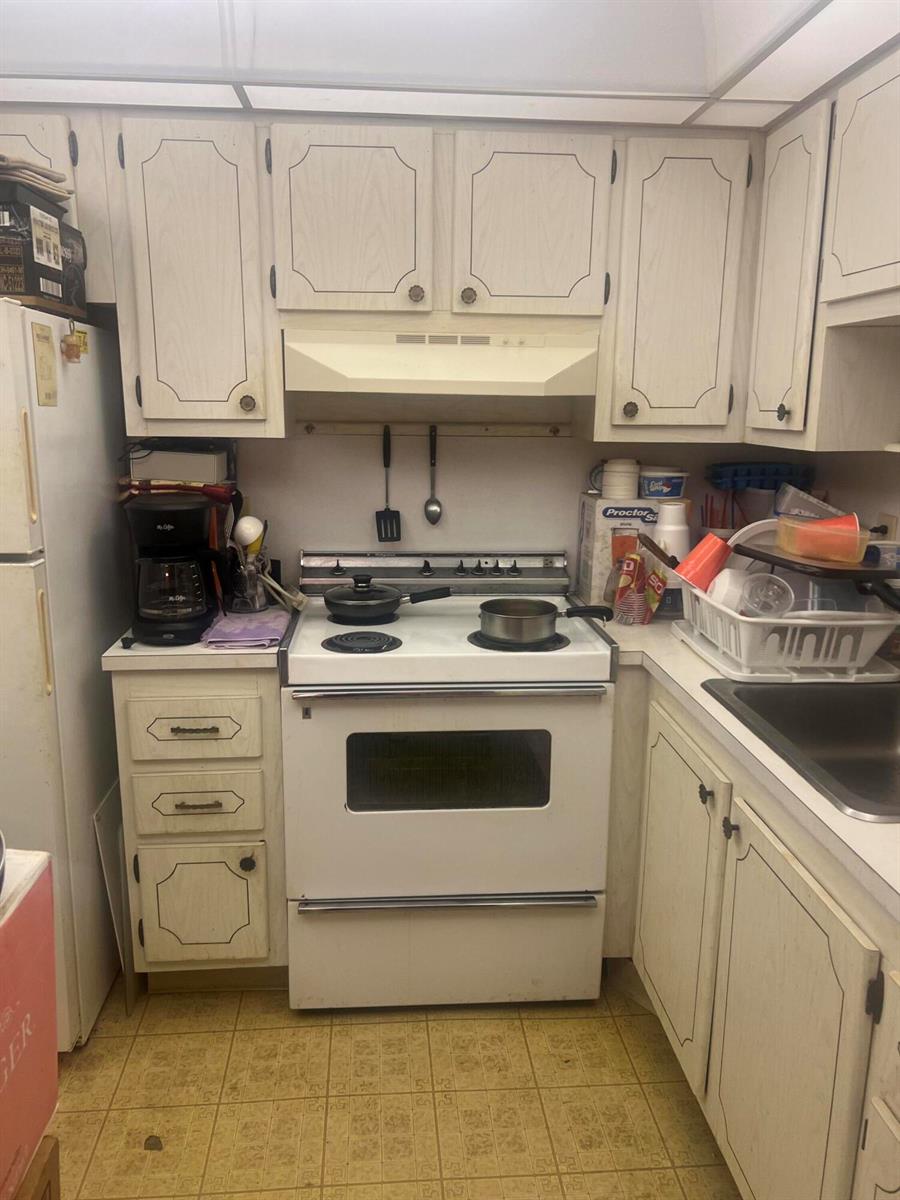 A kitchen features white cabinets, a white stove, and a patterned linoleum floor — 62 Valencia C, Delray Beach FL 33446, DELRAY BEACH, FL